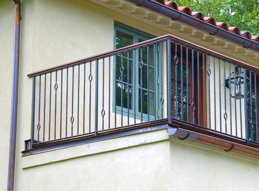 A balcony features a wrought iron railing with eyelet details and a cherry wood top rail.