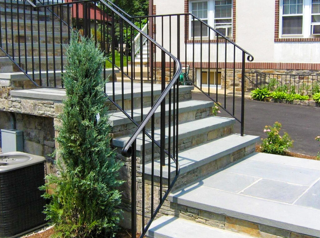 A simple black iron stair rail with square vertical spindles frames a gray flagstone staircase.