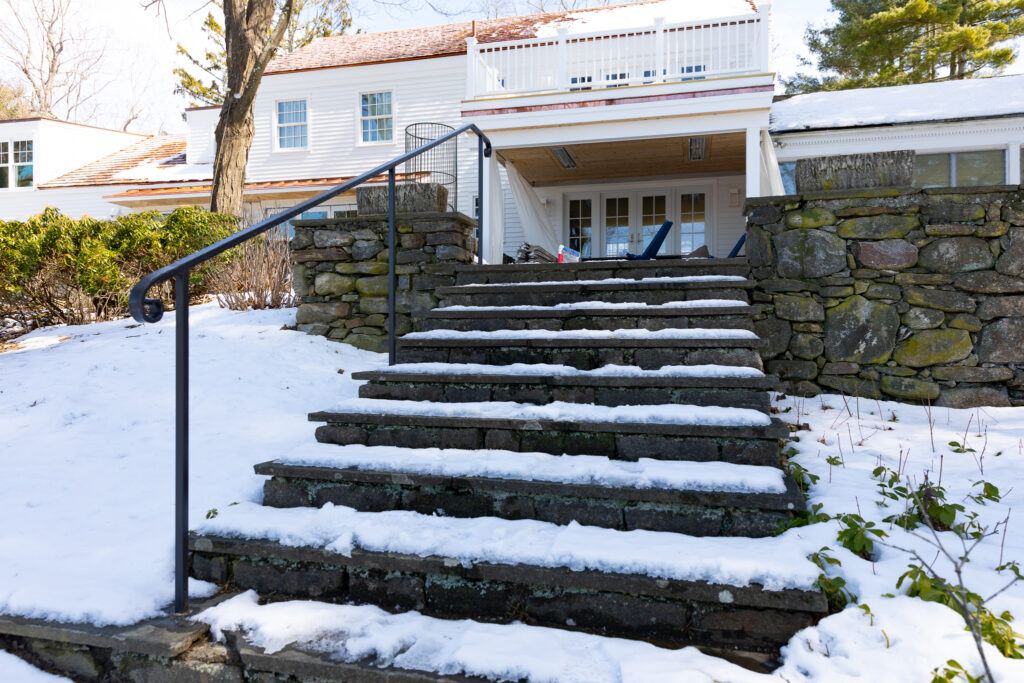 A wrought iron handrail is supported by three posts along one side of dry stone steps leading towards a dry-stack stone wall.