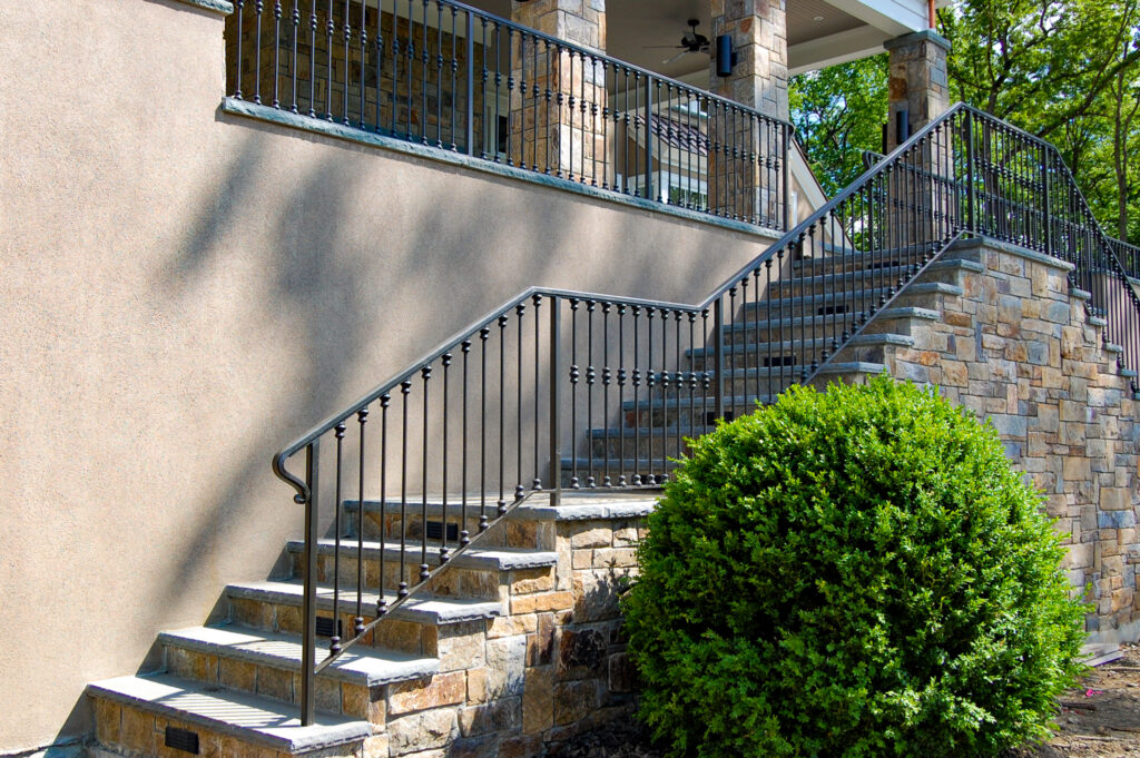 A simple iron railing protects the outdoor stone staircase leading up to an imposing stucco home. 