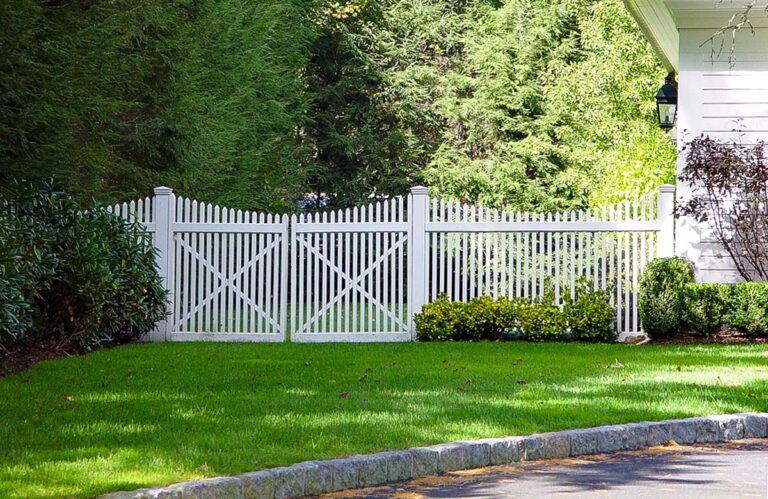 White PVC fencing with scalloped pickets and a walk gate separates the backyard from the side yard next to a home.